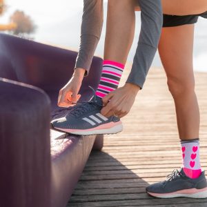 sportive qui fait ses lacets, qui porte des chaussettes de sport techniques, respirantes les raymondes avec des cœurs et des rayures rose fluo, noir, blanc