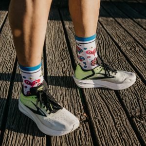 jambes masculines avec des chaussettes de sport techniques respirantes les raymondes modèle grifouille blanches avec des motifs drôles